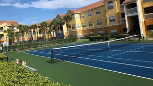 Een tennisbaan omringd door gele gebouwen met rode daken en balkons.