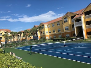 A tennis court surrounded by yellow buildings with red roofs and balconies.