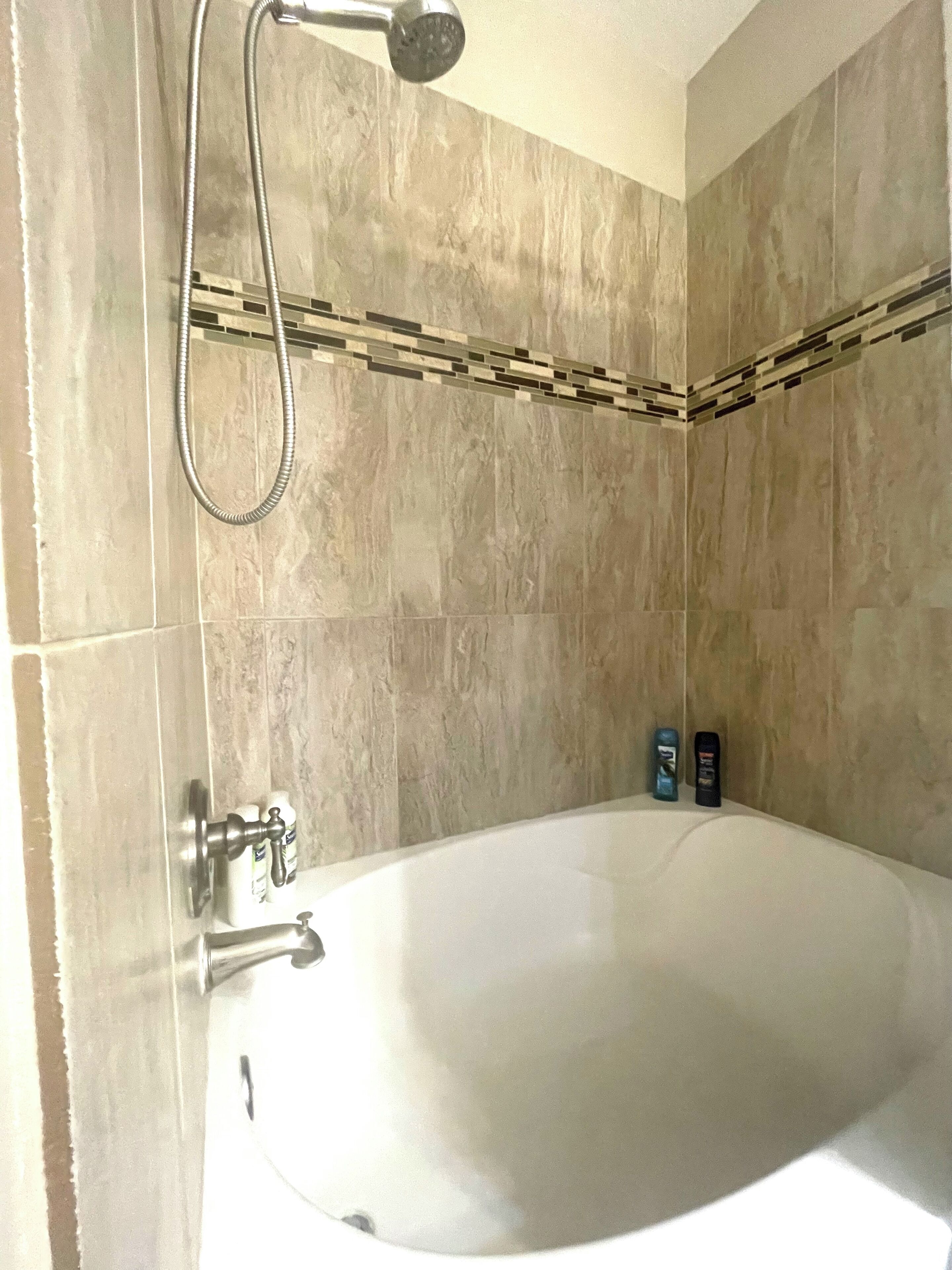 A bathroom with a large bathtub, a showerhead, and toiletries on the side.