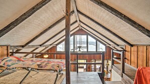 A loft bedroom with a high ceiling, wooden beams, a bed, a window, and a staircase leading to an upper level. - Authentic Retreat w/ Private Dock on Coosa River! (Shelby)