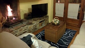 A cozy living room with a stone fireplace, a flat-screen TV, and a wicker basket on a patterned rug.