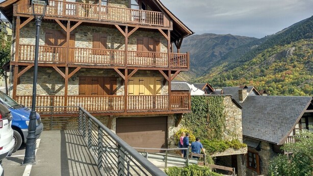 A multi-story wooden building with balconies, set against a mountainous backdrop.