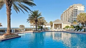 A swimming pool with lounge chairs and palm trees, surrounded by a building with balconies. - BEACHFRONT CONDO IN THE CATALINA TOWER, BEACH CLUB, GULF SHORES!!!!! (Gulf Shores)