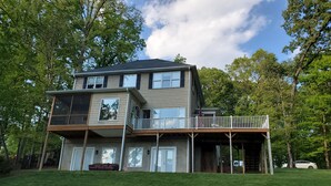 Une maison à deux étages avec un balcon, une véranda et une cour gazonnée.