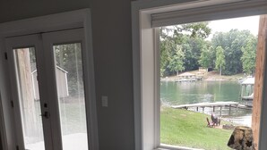 Une chambre à coucher avec un grand lit, une fenêtre donnant sur un lac et une porte équipée de stores.