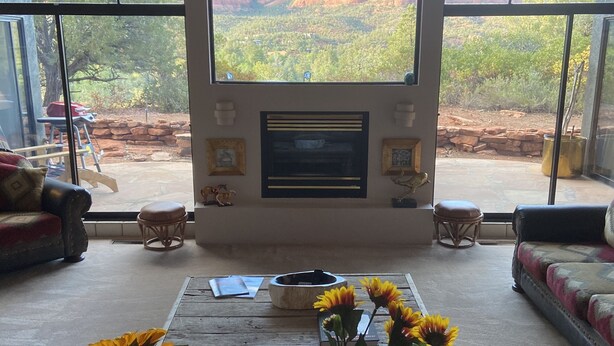 A living room with a fireplace, large windows, and a table with sunflowers. - A COWBOYS CASA--BEST RED ROCK VIEWS IN SEDONA -WALK TO TLAQUEPAQUE & UPTOWN-- (Sedona)