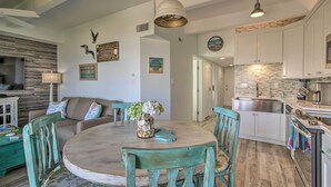 Una cocina moderna con armarios blancos, un lavamanos de acero inoxidable y una mesa de comedor de madera con sillas color turquesa.