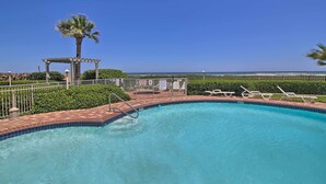 Una piscina con pérgola, sillas de descanso y vistas al océano.