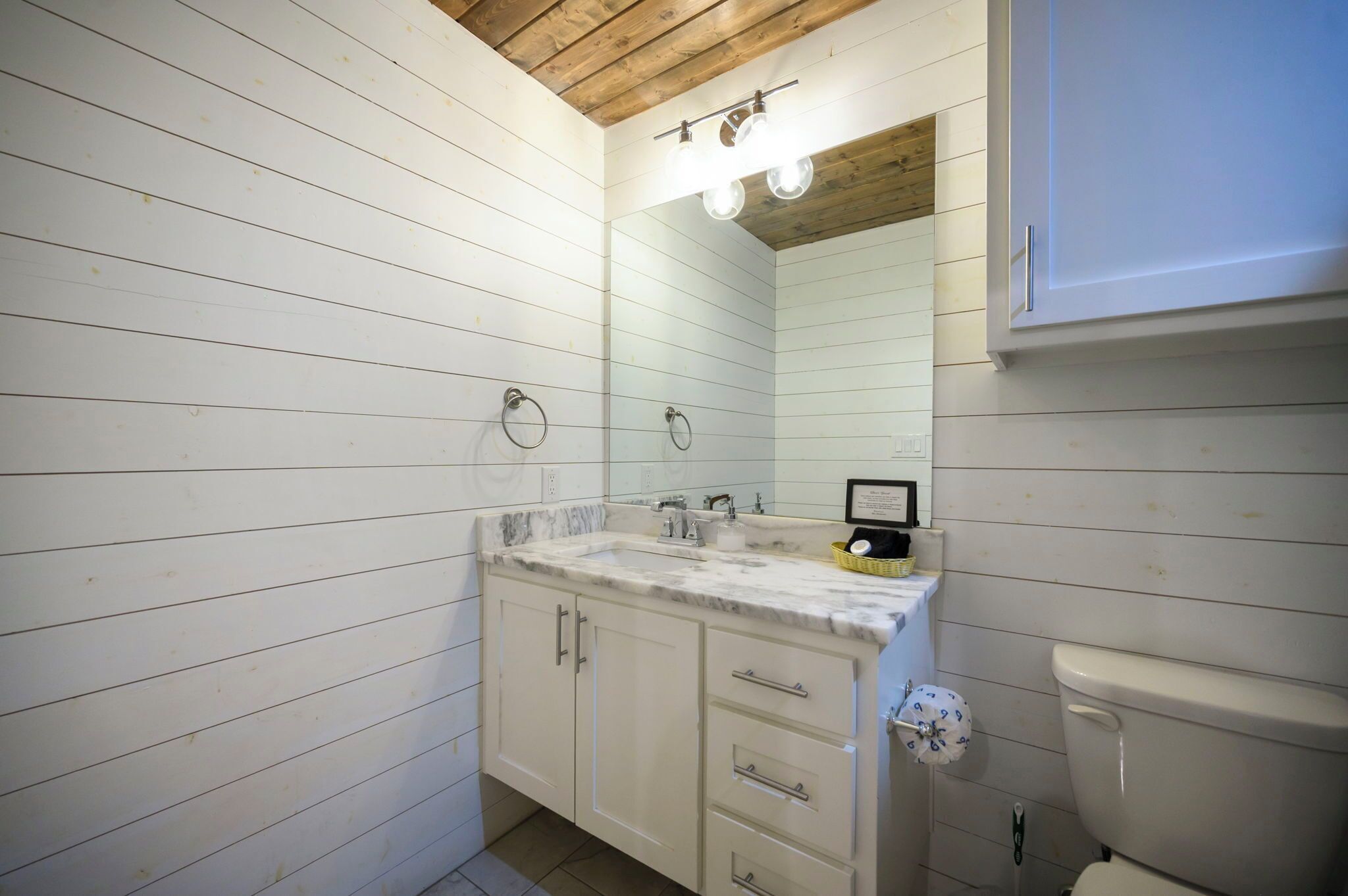 Your rustic-chic bathroom features warm shiplap walls, elegant marble counters, and thoughtful lighting for your morning routine.