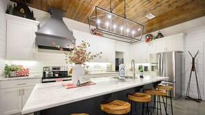 Una cucina moderna con un'isola grande, sgabelli da bar in legno, elettrodomestici in acciaio inossidabile e un elemento decorativo con piante.