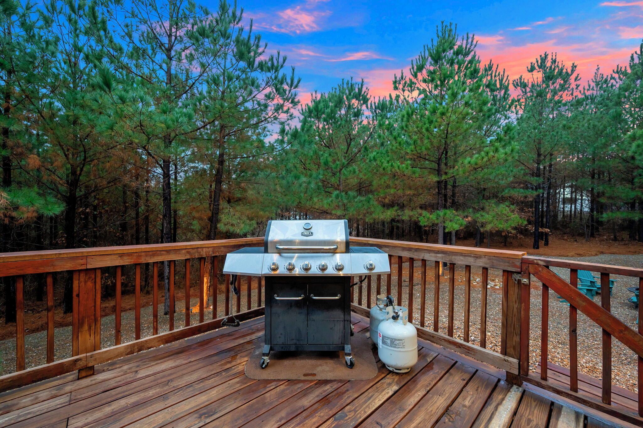 A barbecue grill on a wooden deck with a view of a forest.