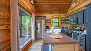 Cocina de cabaña de madera con una isla grande, electrodomésticos de acero inoxidable y vistas al bosque.