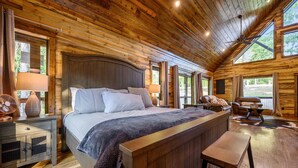 Un dormitorio tipo cabaña de troncos con una cama grande, cabecera de madera, un banco y un ventilador.