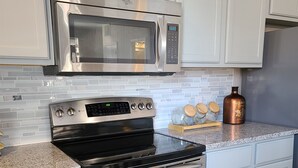 A kitchen with a stainless steel microwave, oven, and stove, white cabinetry, and a granite countertop. - The Lofts of North Main Street (Saint Charles)