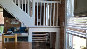 A spacious kitchen with a wooden floor, a white staircase, and a brick wall. - The Lofts of North Main Street (Saint Charles)