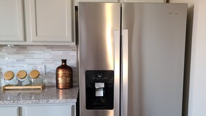 A stainless steel Whirlpool refrigerator with a water dispenser, white cabinetry, and a kitchen counter with jars and a bottle. - The Lofts of North Main Street (Saint Charles)