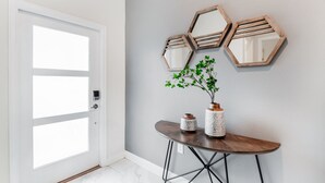 A hallway with a white door, a small round table with a vase and a plant, and three hexagonal mirrors on the wall.