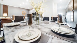 A dining table set with white plates, clear wine glasses, and decorative vases with white flowers.