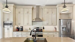 Een moderne keuken met witte kasten, roestvrijstalen apparatuur en hanglampen.