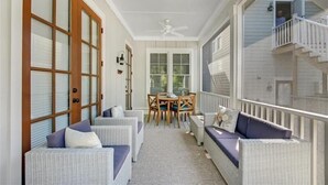 Een overdekt terras met rieten meubels, een plafondventilator en uitzicht op het huis.