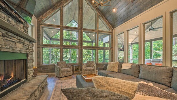 A spacious living room with a stone fireplace, large windows, and a high ceiling. - Perfect for Couples,2 King Master bedrooms, Dry Sauna, Hot Tub, 3 covered decks (Broken Bow)