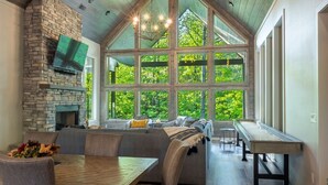 A modern kitchen with a stone fireplace, large windows, and a dining area with a wooden table and chairs. - Perfect for Couples,2 King Master bedrooms, Dry Sauna, Hot Tub, 3 covered decks (Broken Bow)