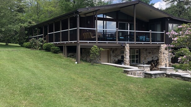 A two-story house with a balcony, stone foundation, and a well-maintained lawn.