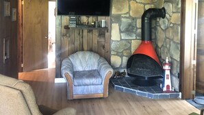 A cozy living room with a stone wall, a fireplace, a television, and a comfortable armchair.