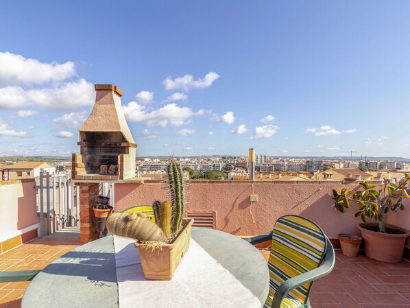 A rooftop terrace with a brick oven, a cactus, and a view of a cityscape.