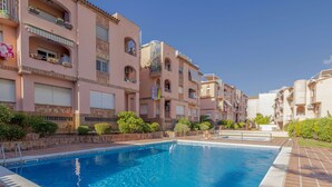 A swimming pool surrounded by multi-story buildings with balconies, a clear sky, and a tiled walkway. - Cosy apartment for 4 guests with pool, A/C, WIFI, TV and terrace (Torredembarra)