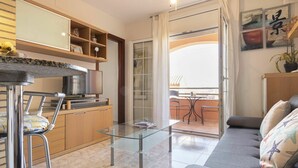 A modern living room with a glass coffee table, a sofa, and a kitchen area with a TV and cabinets. - Cosy apartment for 4 guests with pool, A/C, WIFI, TV and terrace (Torredembarra)