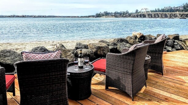 Eine Holzterrasse mit Korbmöbeln und einem Tisch, gedeckt mit Weingläsern und einer Weinflasche.