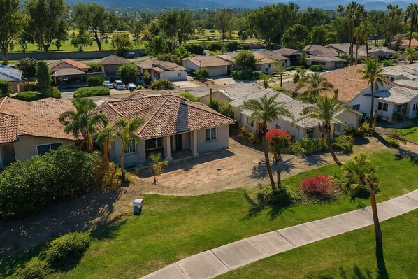 A residential area with houses, palm trees, and a well-maintained lawn.