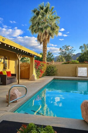 A pool area with a palm tree, a covered seating area, and a mountain view.