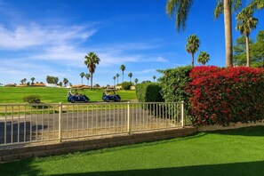 Een golfbaan met twee golfkarren, palmbomen en een haag met rode bloemen.