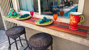 A bar area with wicker stools, a colorful woven mat, and a large decorative pitcher.