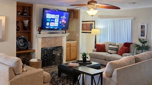 A living room with a fireplace, television, ceiling fan, and two sofas.