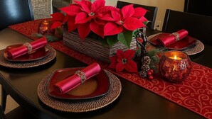 A dining table set with red napkins, a centerpiece of red poinsettias, and red candle holders.
