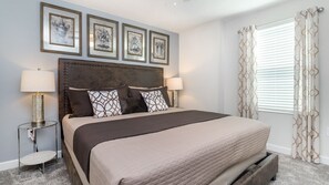 A neatly arranged bedroom with a large bed, two bedside lamps, a round side table, and a headboard with decorative molding.