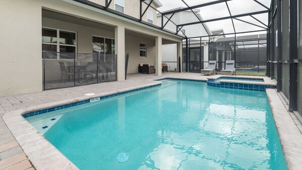 A swimming pool with a glass-enclosed patio area, outdoor seating, and a covered section with a view of the pool.