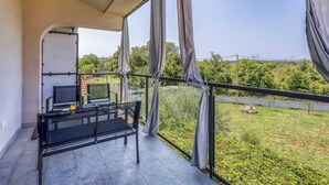 Ein Balkon mit Tisch, Stühlen und Fernseher. Der Balkon bietet Blick auf eine grüne Landschaft mit Bäumen und blauem Himmel.
