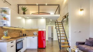 Eine moderne Küche mit weißen Schränken, einem roten Kühlschrank und einer Holztreppe zu einer oberen Ebene.