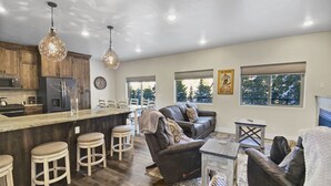 A spacious living area with a large dark wood floor, a leather sofa, a coffee table, and a kitchen area with wooden cabinets and a bar.