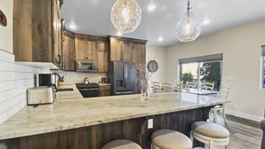 A modern kitchen with wooden cabinets, a marble countertop, and a central island with stools.