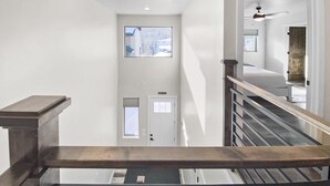 A staircase with a wooden handrail leading to a landing. A door with a window is visible on the landing, and a ceiling fan is mounted on the wall.