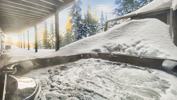 A hot tub with a view of snow-covered trees and a clear sky.