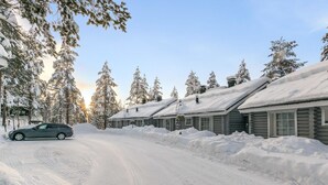 Uma estrada coberta de neve que leva a uma fileira de cabanas de madeira com neve nos telhados e árvores.