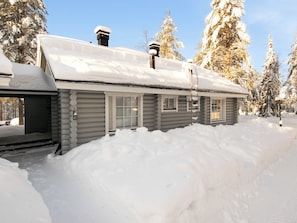 En hytte med snedækket tag, skorsten og en veranda.