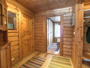 Un intérieur en bois avec un couloir menant à une porte, une petite étagère et un tapis à motifs.