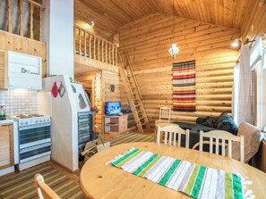Un intérieur chaleureux de chalet en bois, comprenant une cuisine, un coin repas et une chambre à coucher située en mezzanine.